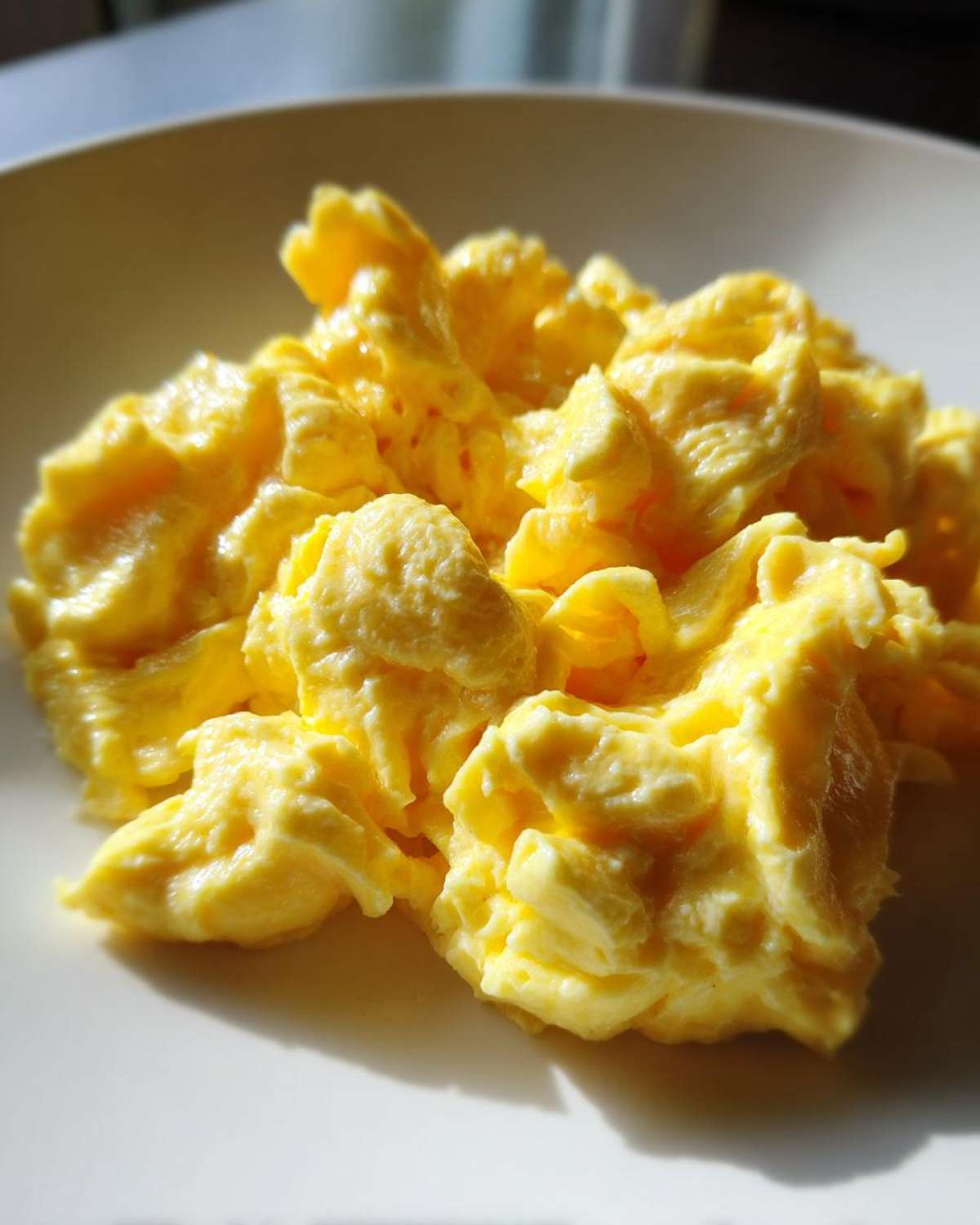 Close-up of bright yellow, fluffy scrambled eggs served on a white plate.
