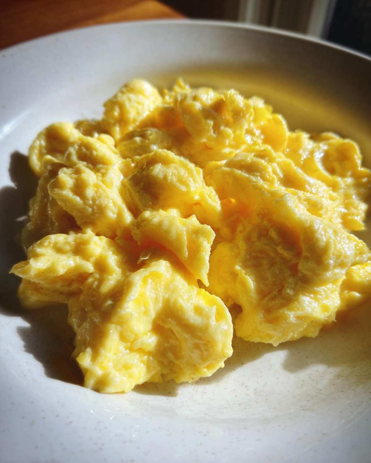 Close-up of perfectly cooked, fluffy scrambled eggs with a creamy texture served in a light-colored bowl.