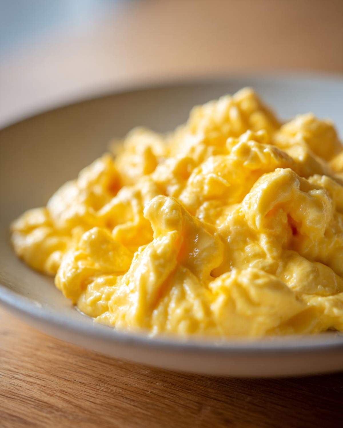 A close-up view of creamy, bright yellow, fluffy scrambled eggs served in a light-colored bowl.