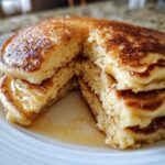 Close-up of a stack of fluffy sourdough pancakes cut open, drizzled with syrup on a white plate.
