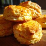 A stack of fluffy sweet potato biscuits with a shiny glaze, sitting on a wooden cutting board.