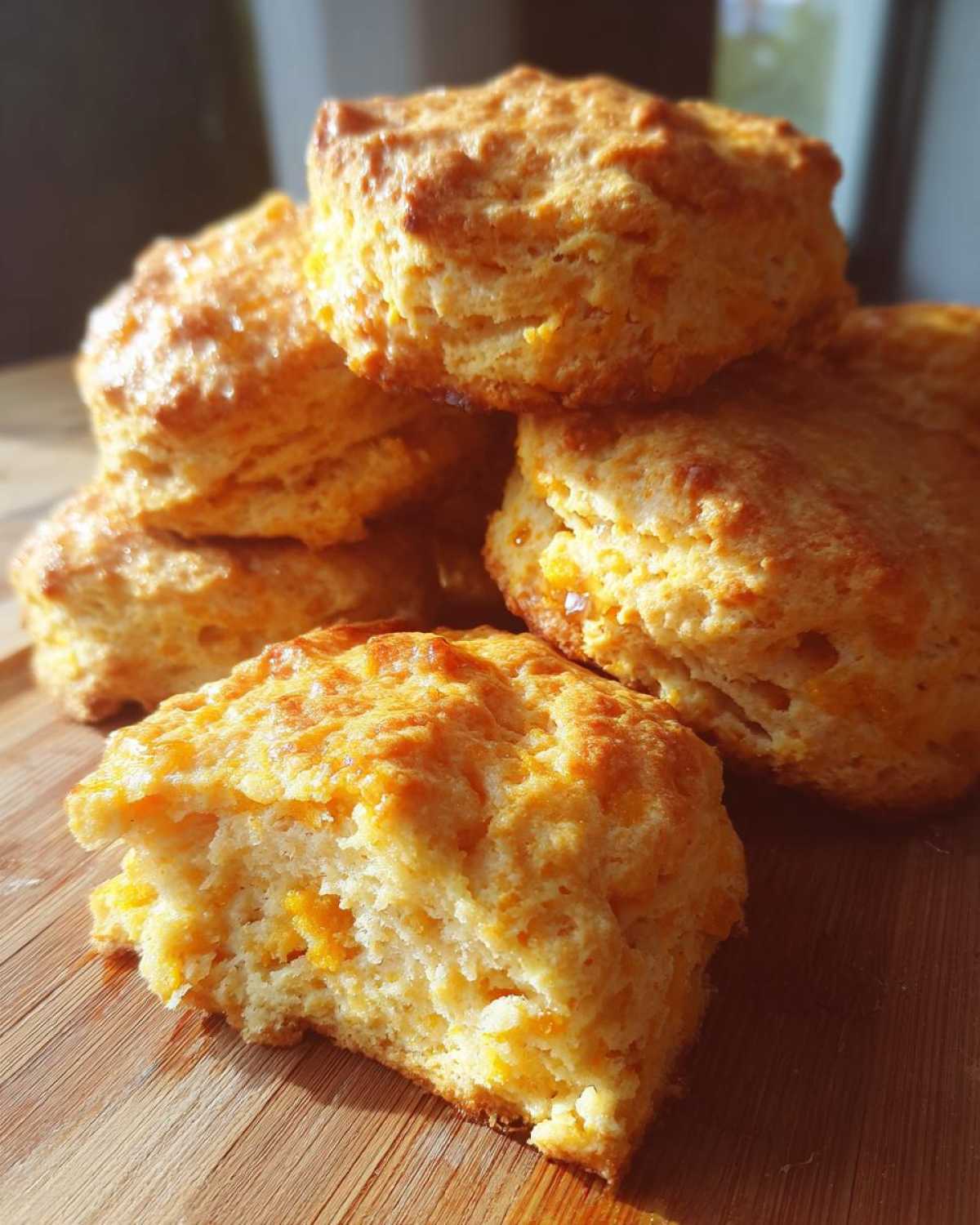 A stack of golden brown, fluffy sweet potato biscuits, with one broken open showing the soft interior.