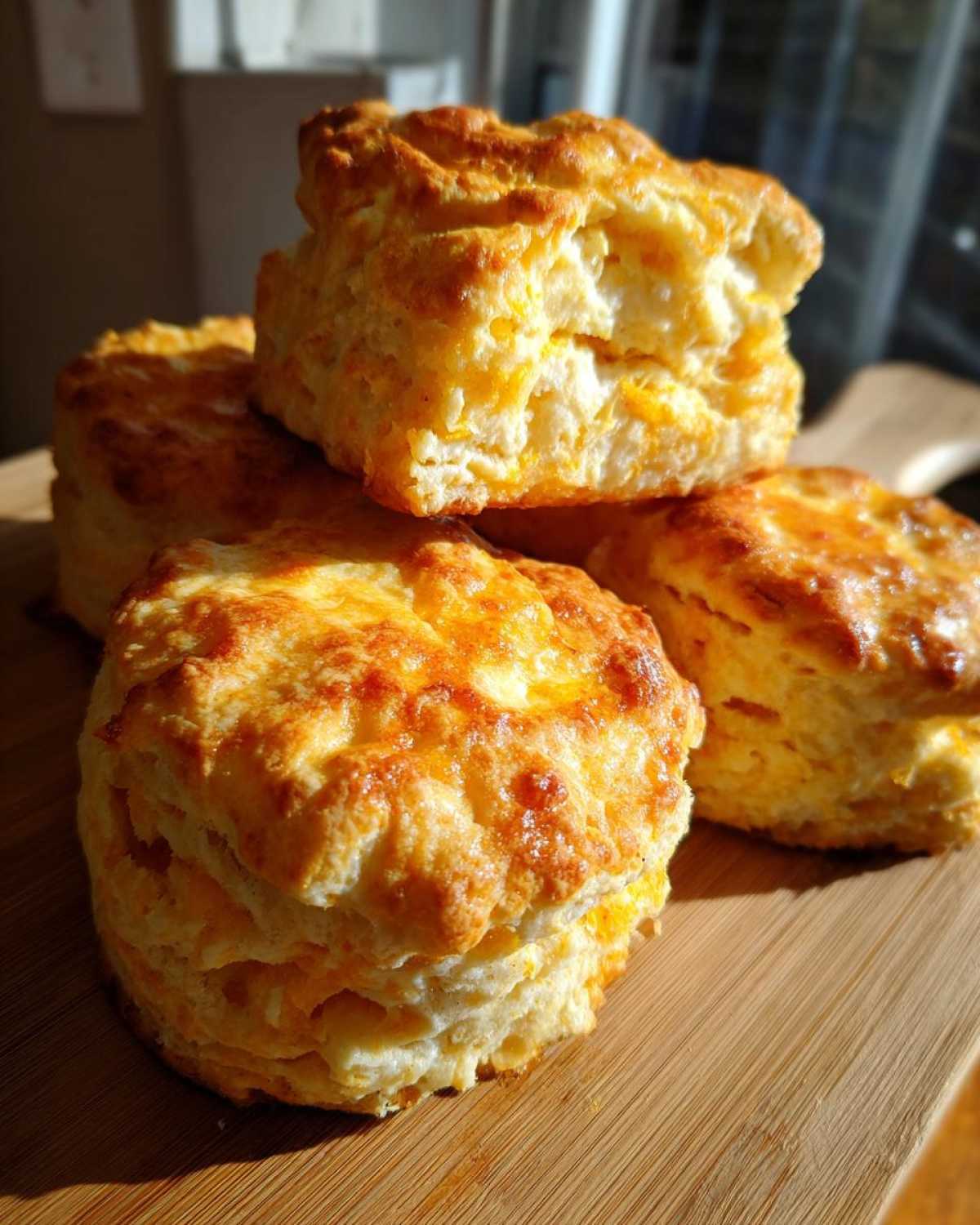 A stack of four golden brown, fluffy sweet potato biscuits with flaky layers, sitting on a wooden board.