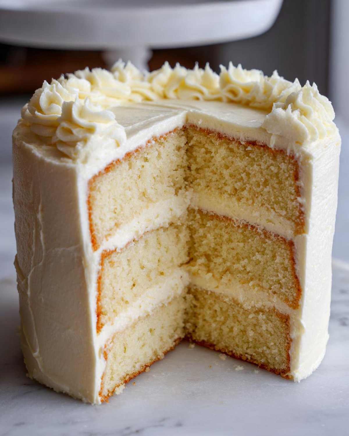 Cross-section of a fluffy vanilla cake recipe showing three layers and white vanilla buttercream frosting.