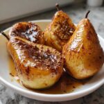 Four perfectly glazed baked pears topped with brown sugar and spices served in a white bowl.