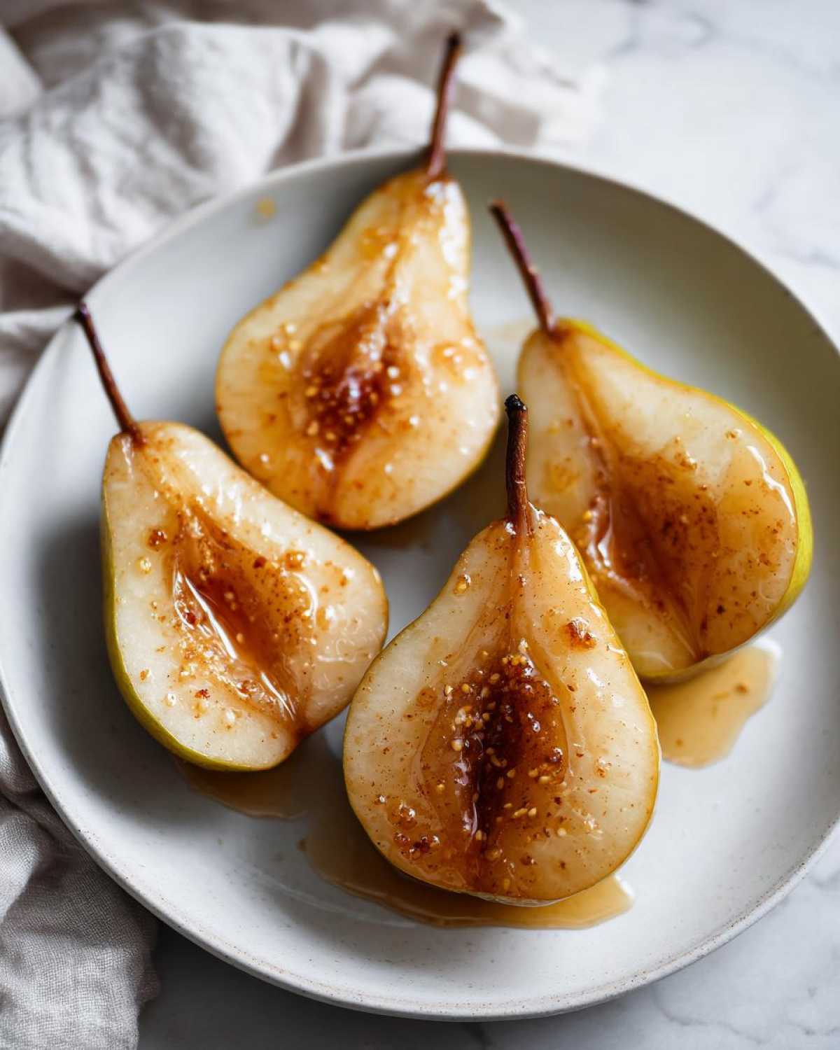 Four halves of baked pears drizzled with a sweet, spiced glaze, served on a light plate.