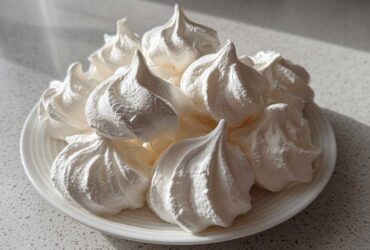 A pile of perfectly piped, bright white meringue cookies displayed on a small white plate.