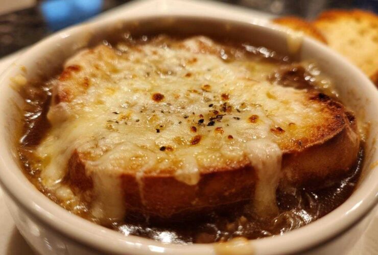 Close-up of a bowl of rich french onion soup topped with a thick layer of melted, browned cheese over toasted bread.
