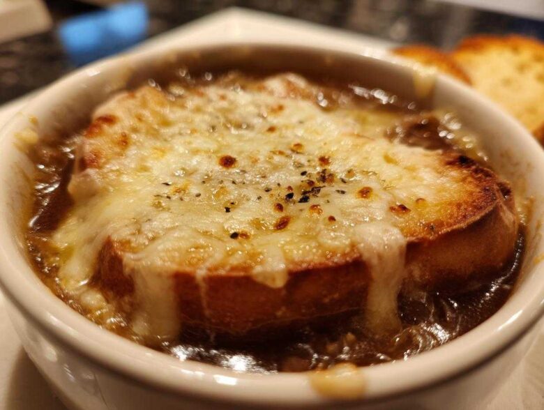 Close-up of a bowl of rich french onion soup topped with a thick layer of melted, browned cheese over toasted bread.