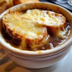 Close-up of a bowl of rich french onion soup topped with melted, bubbly cheese over toasted bread.