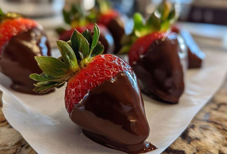 A close-up of fresh chocolate covered strawberries resting on parchment paper, showcasing the glossy dark chocolate coating.