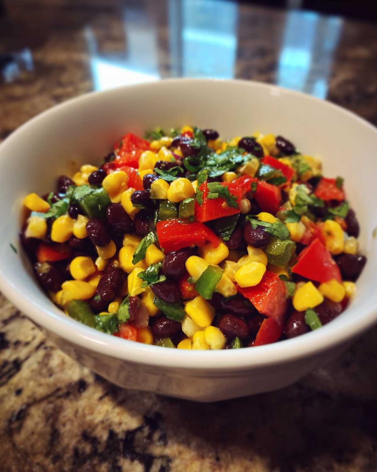 Close-up of vibrant cowboy caviar featuring black beans, corn, red peppers, and cilantro in a white bowl.