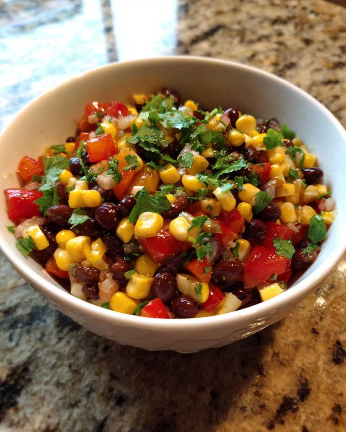 Close-up of vibrant cowboy caviar featuring black beans, corn, diced tomatoes, and cilantro in a white bowl.