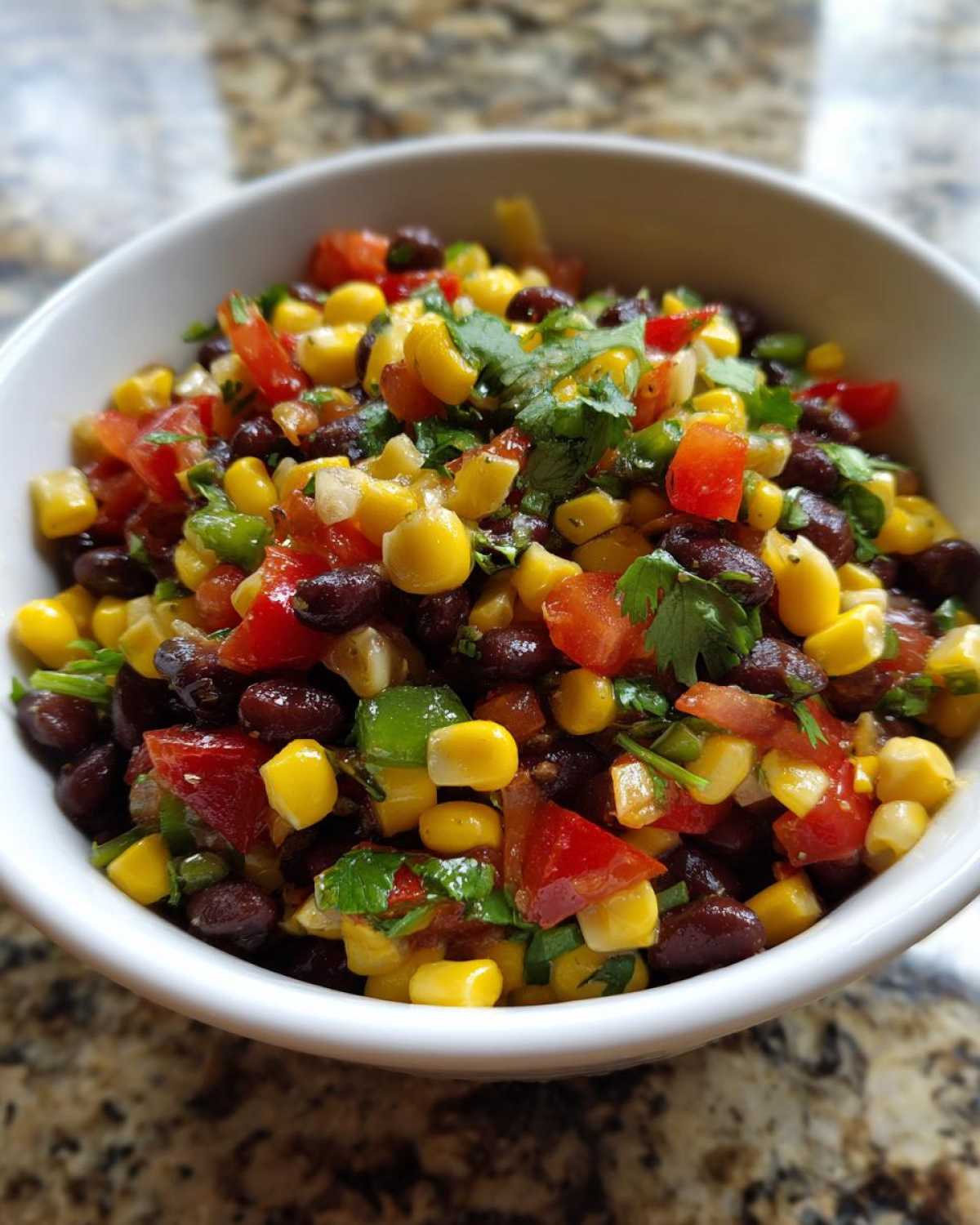 Close-up of vibrant cowboy caviar salad featuring black beans, corn, tomatoes, and cilantro in a white bowl.