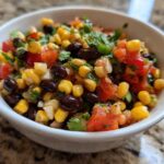 Close-up of vibrant cowboy caviar featuring corn, black beans, diced tomatoes, and cilantro in a small white bowl.