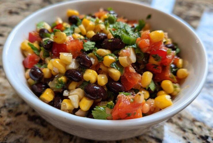 Close-up of vibrant cowboy caviar featuring corn, black beans, diced tomatoes, and cilantro in a small white bowl.