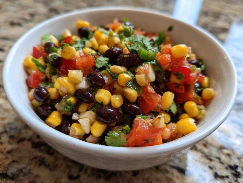 Close-up of vibrant cowboy caviar featuring corn, black beans, diced tomatoes, and cilantro in a small white bowl.