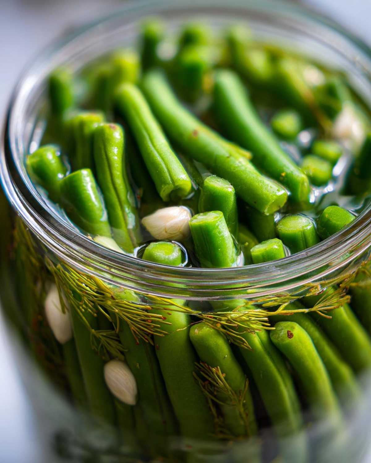 Close-up of bright green dilly beans packed tightly in a glass jar with fresh dill sprigs and garlic cloves.