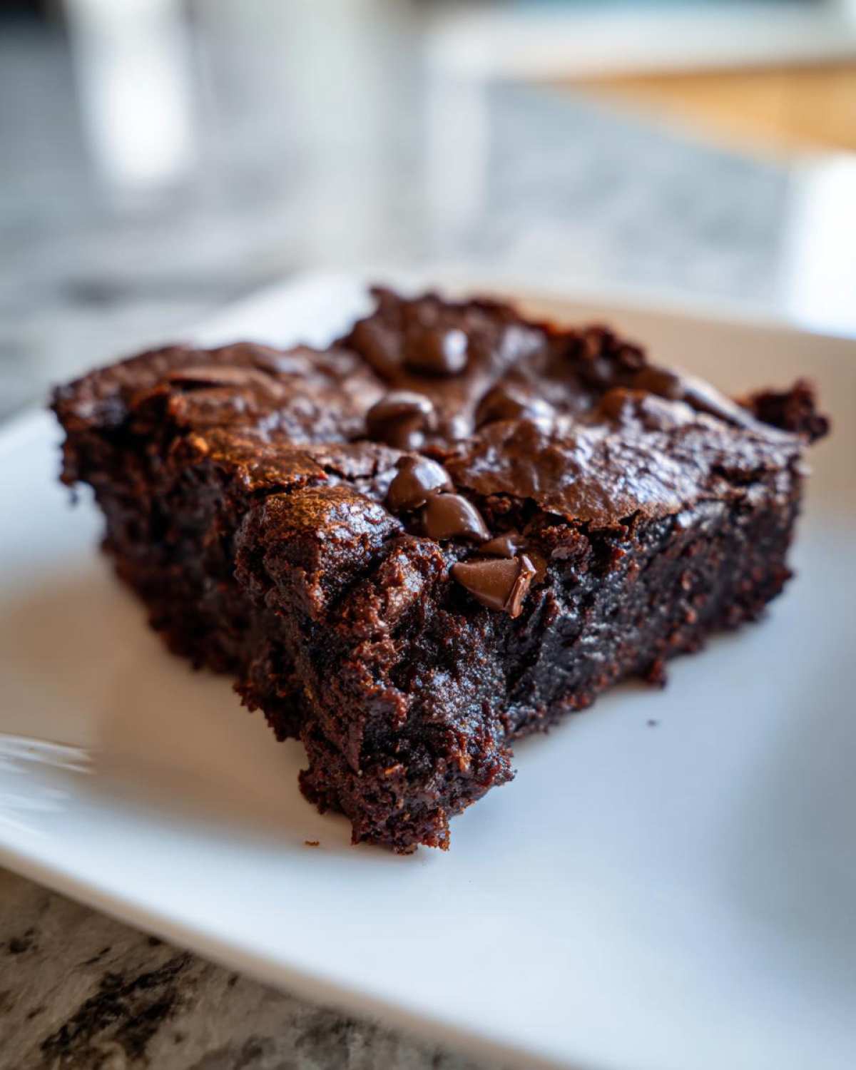 Close-up of a fudgy slice of black bean brownies topped with melted chocolate chips on a white plate.
