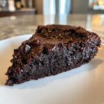 A close-up, fudgy slice of black bean brownies topped with melted chocolate chips on a white plate.