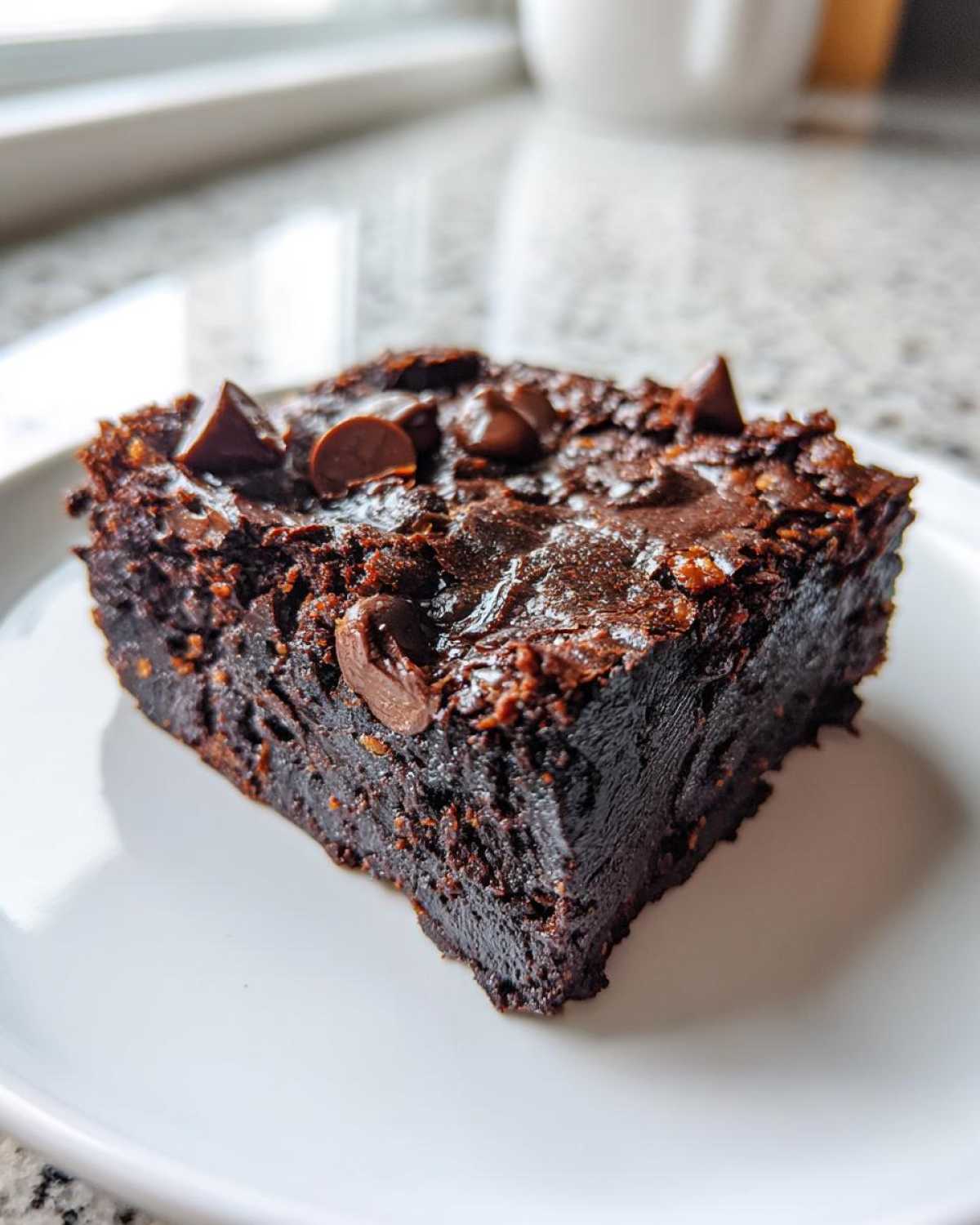 Close-up of a fudgy square of black bean brownies topped with melted chocolate chips on a white plate.