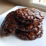 A stack of three rich, fudgy chocolate brownie cookies with shiny, cracked tops.