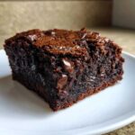 Close-up of a rich, dark, fudgy slice of gingerbread brownies studded with melted chocolate chips on a white plate.