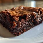 Close-up of a fudgy, dark chocolate gingerbread brownie with a crackly top, sitting on a white plate.