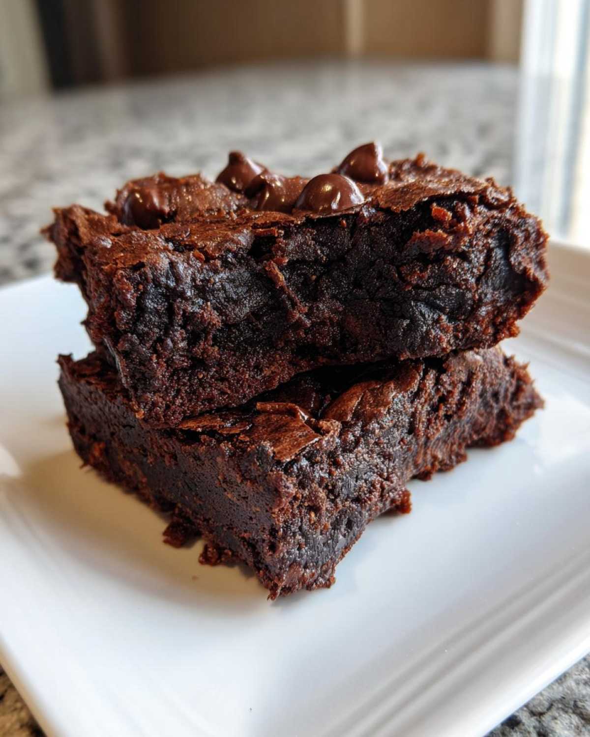 Two stacked, fudgy gingerbread brownies topped with melted chocolate chips resting on a white plate.