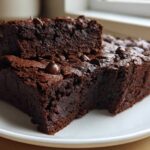 Two rich, dark fudgy sweet potato brownies stacked on a white plate, topped with melted chocolate chips.