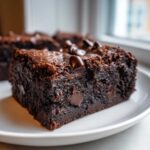 Close-up of a fudgy, dark chocolate sweet potato brownies slice topped with melted chocolate chips.