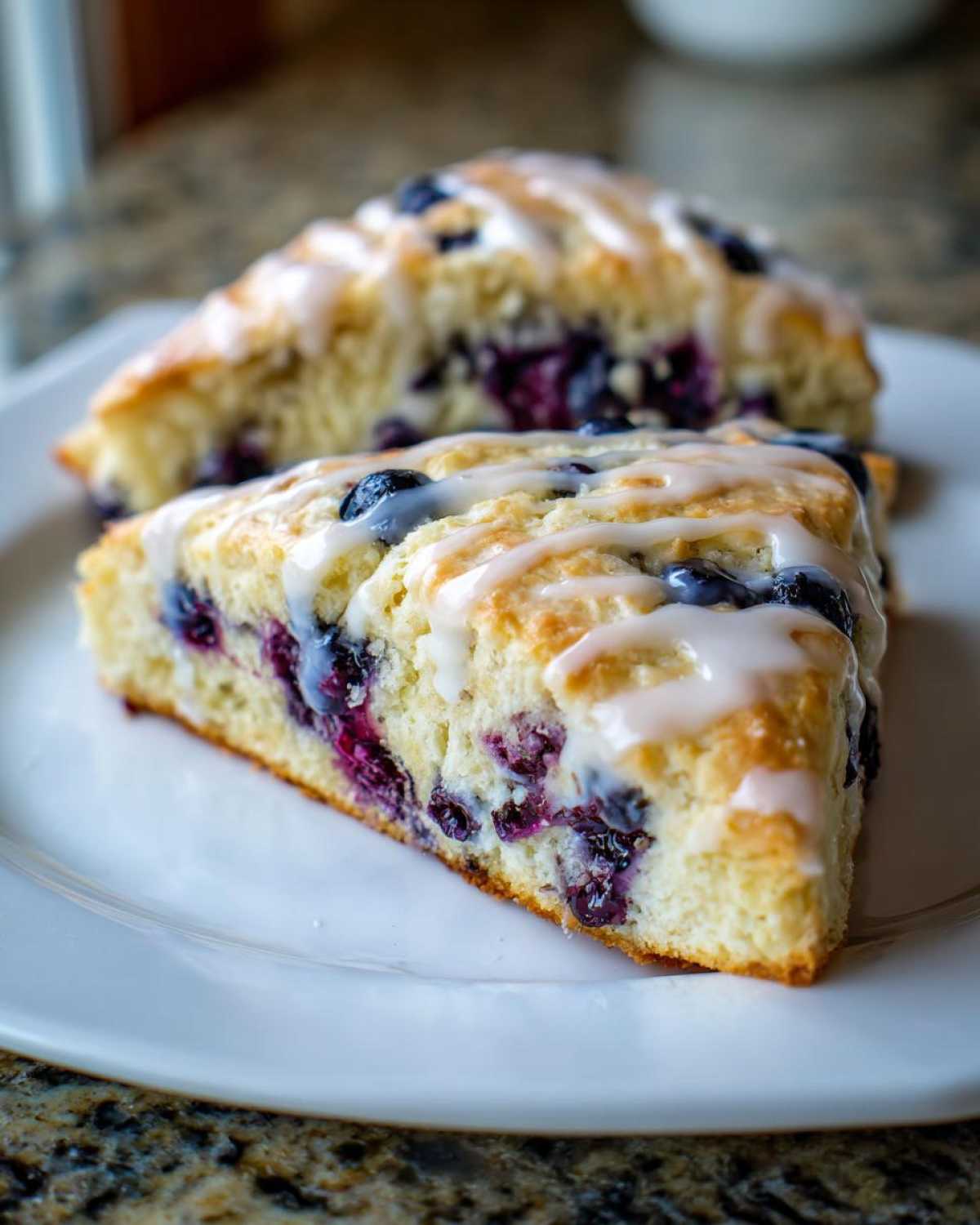 Two triangular blueberry scones, drizzled with white glaze, sitting on a white plate.