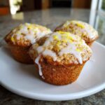 Three freshly baked lemon poppy seed muffins topped with white glaze and bright yellow lemon zest.