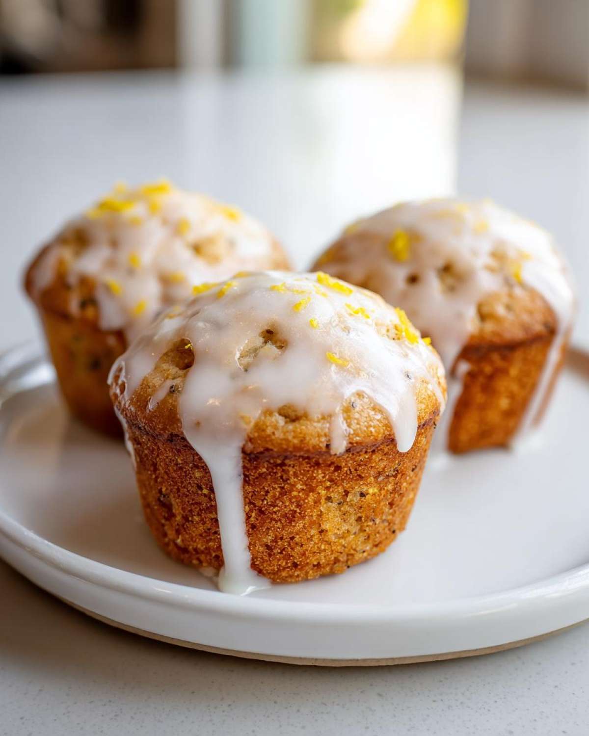 Three freshly baked lemon poppy seed muffins topped with thick white glaze and lemon zest.