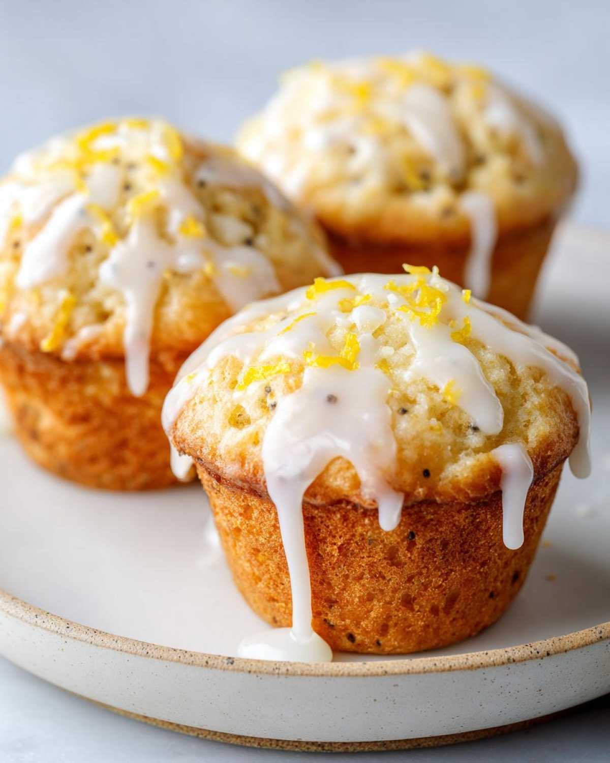 Close-up of three delicious lemon poppy seed muffins topped with thick white glaze and lemon zest.