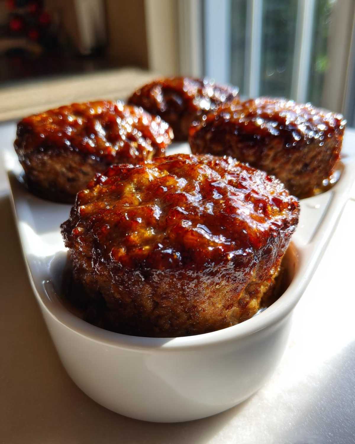 Close-up of four shiny, glazed mini meatloaf portions served in a white dish.
