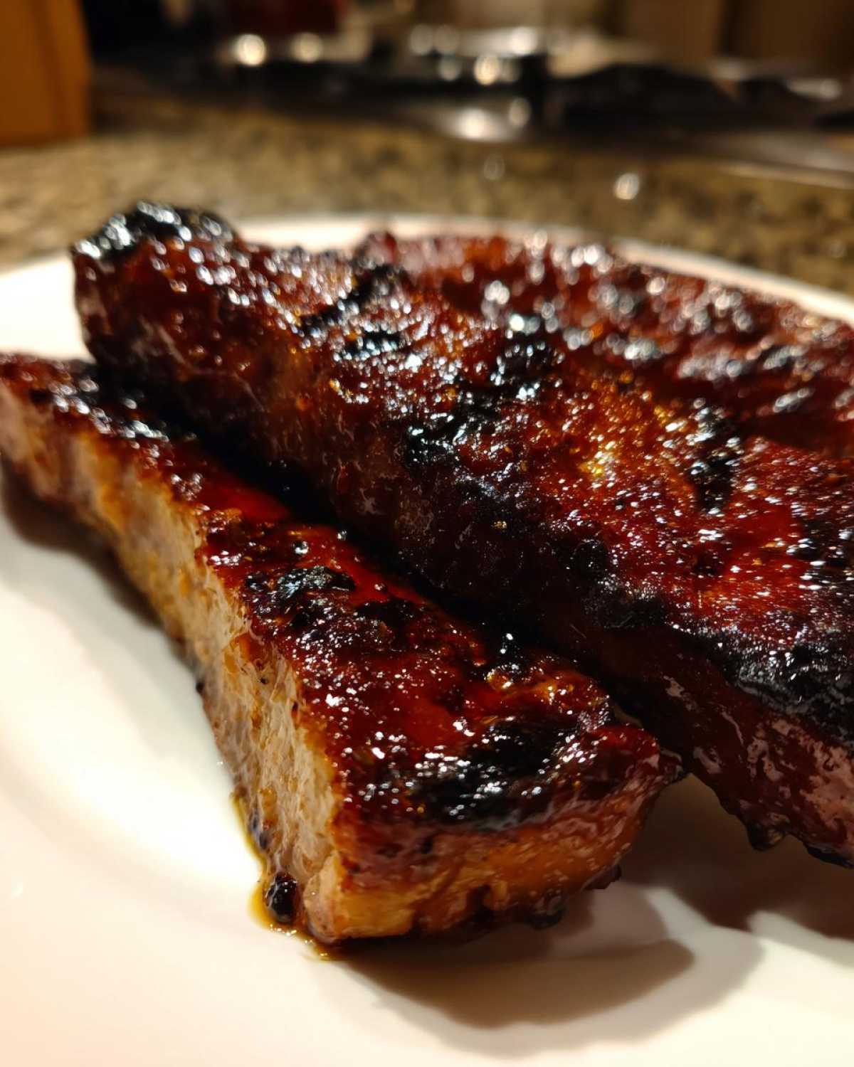 Close-up of two thick, glazed pork steak pieces with a dark, caramelized crust, served on a white plate.