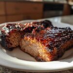 Two thick, juicy pieces of glazed pork steak recipe resting on a white plate, showing a caramelized, dark red sauce.