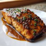 Close-up of a perfectly cooked salmon fillet coated in a sticky, brown glaze and topped with fresh parsley.