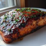 A beautifully glazed salmon fillet with a dark, shiny coating and sprinkled with green herbs.