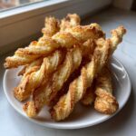 A pile of golden, flaky, twisted cheese straws recipe pastries stacked on a white plate.