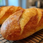Close-up of a golden brown, crusty French bread loaf cooling on a wire rack.