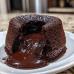 Close-up of a freshly baked chocolate lava cake with the molten center oozing out onto a white plate.