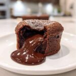Close-up of a perfectly baked chocolate lava cake with molten center oozing onto a white plate.