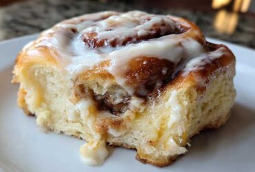 A close-up shot of a soft, freshly baked cinnamon roll topped with dripping white icing, showing the sweet cinnamon swirl inside.