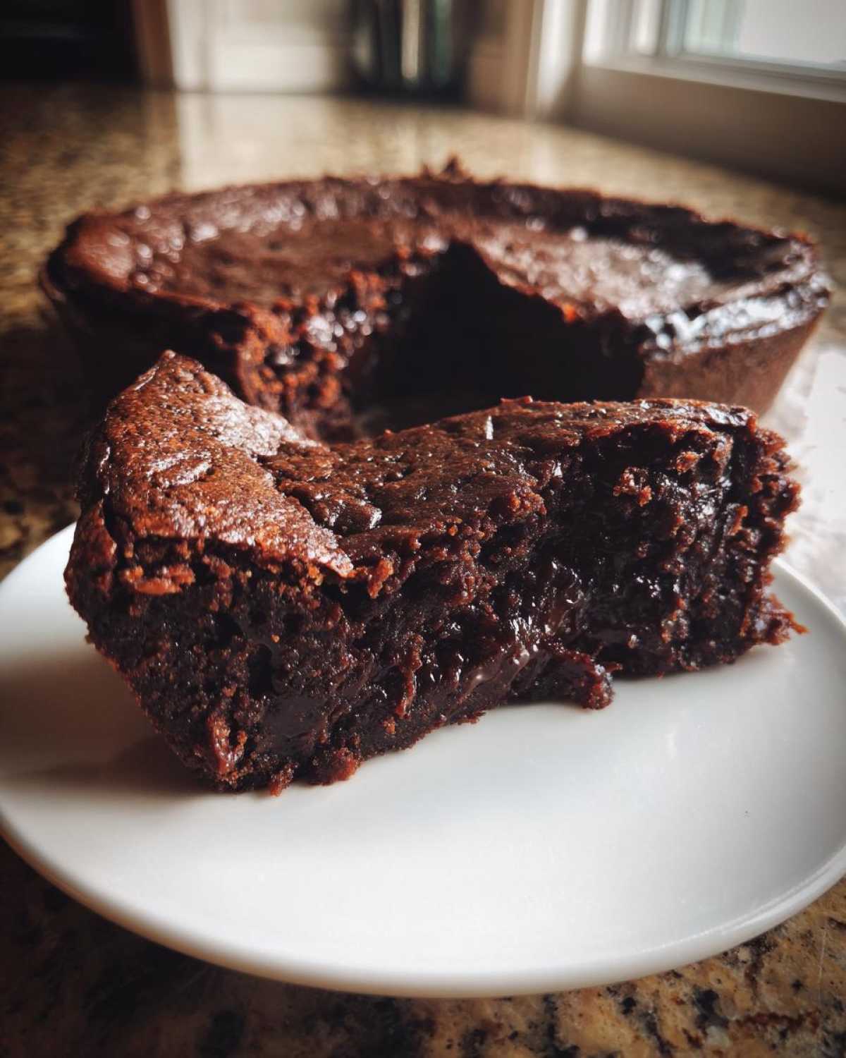 A close-up of a gooey, rich slice of hot fudge pie served on a white plate.