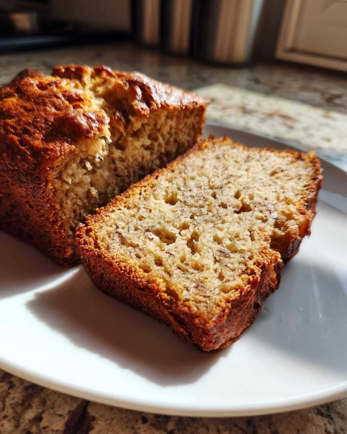 Close-up of a slice of moist greek yogurt banana bread with a golden-brown crust, resting on a white plate.