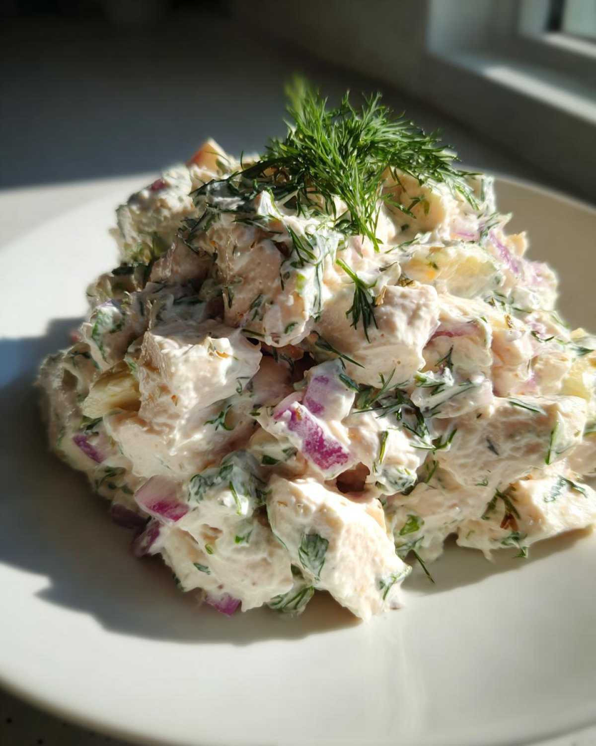 Close-up of a serving of greek yogurt chicken salad mixed with red onion and topped with fresh dill.