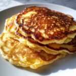 A close-up stack of golden-brown greek yogurt pancakes with beautifully browned, lacy edges.