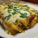 Close-up of baked green chile chicken enchiladas topped with melted white cheese and fresh cilantro.